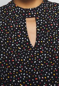 Tessuto nero con un motivo a pois di vari colori, caratterizzato da un collo a chiave e un design del colletto strutturato.