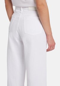 Pantaloni bianchi a vita alta con una vestibilità ampia, dotati di tasche posteriori e una superficie liscia. Design semplice con dettagli di stile minimalisti.