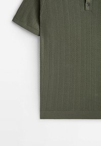 Polo manches courtes vert olive avec motif tricoté texturé, col et poignets côtelés, et fermeture à boutons sur le devant.
