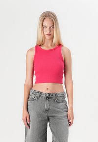 Tett ribbet kort topp i lys rosa, kombinert med høyt liv, lysegrå denimbukser med en lett slitt tekstur.