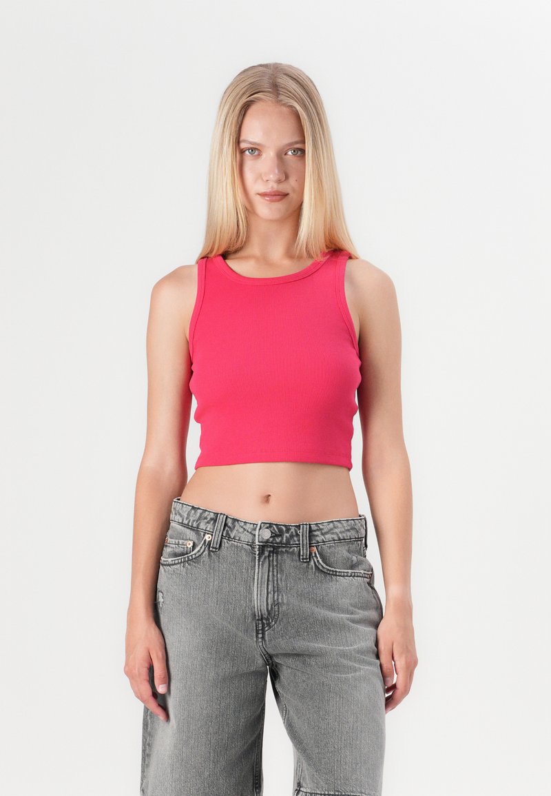 Tett ribbet kort topp i lys rosa, kombinert med høyt liv, lysegrå denimbukser med en lett slitt tekstur.