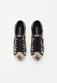 Beige textilní tenisky s černým šněrováním, s logem a bílé gumové podešve, navržené pro volný čas.