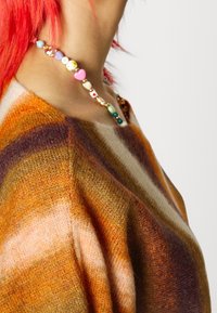 Färgglad pärlhalsband med hjärtan och olika former, bärs med en brun och orange randig, texturerad tröja.