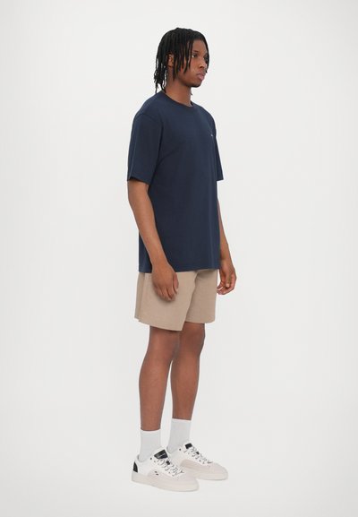 T-shirt à manches courtes navy, shorts beiges, baskets blanches et chaussettes montantes. Le T-shirt a une coupe décontractée ; les matériaux semblent légers et respirants.