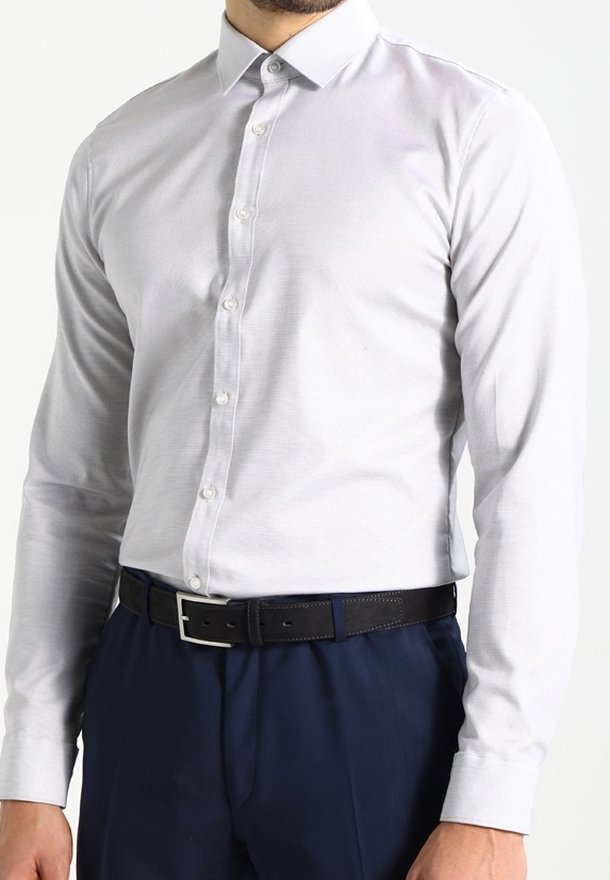 Chemise gris clair à manches longues avec un col boutonné, design ajusté, associée à un pantalon bleu marine et une ceinture en cuir noir avec une boucle en argent.