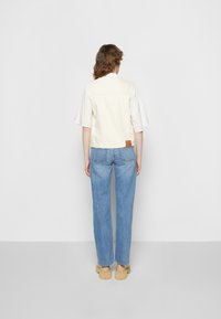 Casaco de ganga creme cortado com mangas curtas, etiqueta de pele bege na parte de trás. Combinado com jeans de perna reta azul claro e calçado bege.