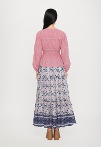 Rot-weiße gestreifte Schürzenoberteil mit Ballonärmeln, kombiniert mit einem langen Blumenrock mit blau-rosa Mustern und einem blauen Saum.