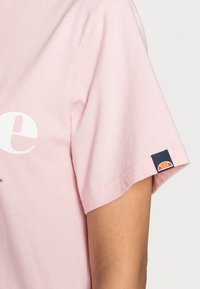 Pink cotton t-shirt with a rounded neckline, featuring a large white logo on the front and a small logo patch on the left sleeve.