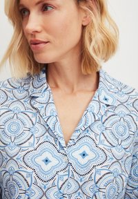 Korte mouwen shirt in lichtblauw met een bloemmotief met intricaten ontwerpen en zwarte accenten, gemaakt van een zachte stof.