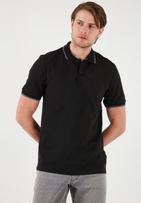 Černé polo tričko vyrobené z bavlněné směsi, s dvouknoflíkovou légou a šedým lemem na límci a rukávech. Hladká textura, krátké rukávy.