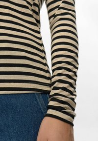 Langsleeve top met zwart en beige horizontale strepen. Heeft een getailleerde pasvorm en een zachte textuur, gecombineerd met blauwe denim jeans.