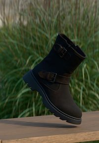 Svarte ankelstøvler laget av semsket skinn med en matt finish. Har to remmer med spenner, en kraftig svart såle og et avslappet design.