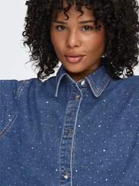 Camicia di jeans con bottoni, caratterizzata da un colletto classico, borchie argentate e tessuto blu scuro con puntini azzurri sparsi.