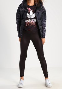 Svart puffjacka med blommönster, svart t-shirt med grafisk design och vit logotyp, svarta leggings och vita sneakers.
