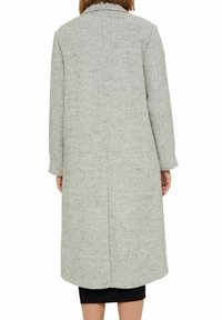 Person wearing a long, textured light gray wool coat with long sleeves, viewed from behind against a white background.