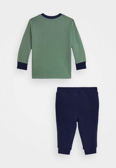 Zelený top s dlouhým rukávem a námořnickými manžetami v kombinaci s námořnickými kalhotami. Obě jsou vyrobeny z měkké bavlny a mají jednoduchý design bez vzorů.