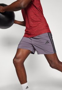 Gray athletic shorts with black side stripes and Adidas logo, paired with a red textured short-sleeve top, tight-fitting and lightweight.