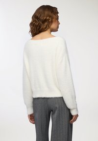 Maglione bianco morbido con una vestibilità ampia, scollo largo e maniche lunghe. Abbinato a pantaloni grigi a spina di pesce con texture.