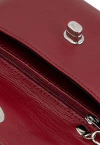 Notranjost rdeče usnjene torbice z zaponko srebrne barve, vidno zadrgo z rdečim šivom in gladko, teksturirano površino.