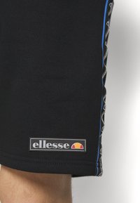 Shorts de sport noirs en tissu doux avec une bande latérale bleue et un patch logo avec un graphisme coloré près de l'ourlet.