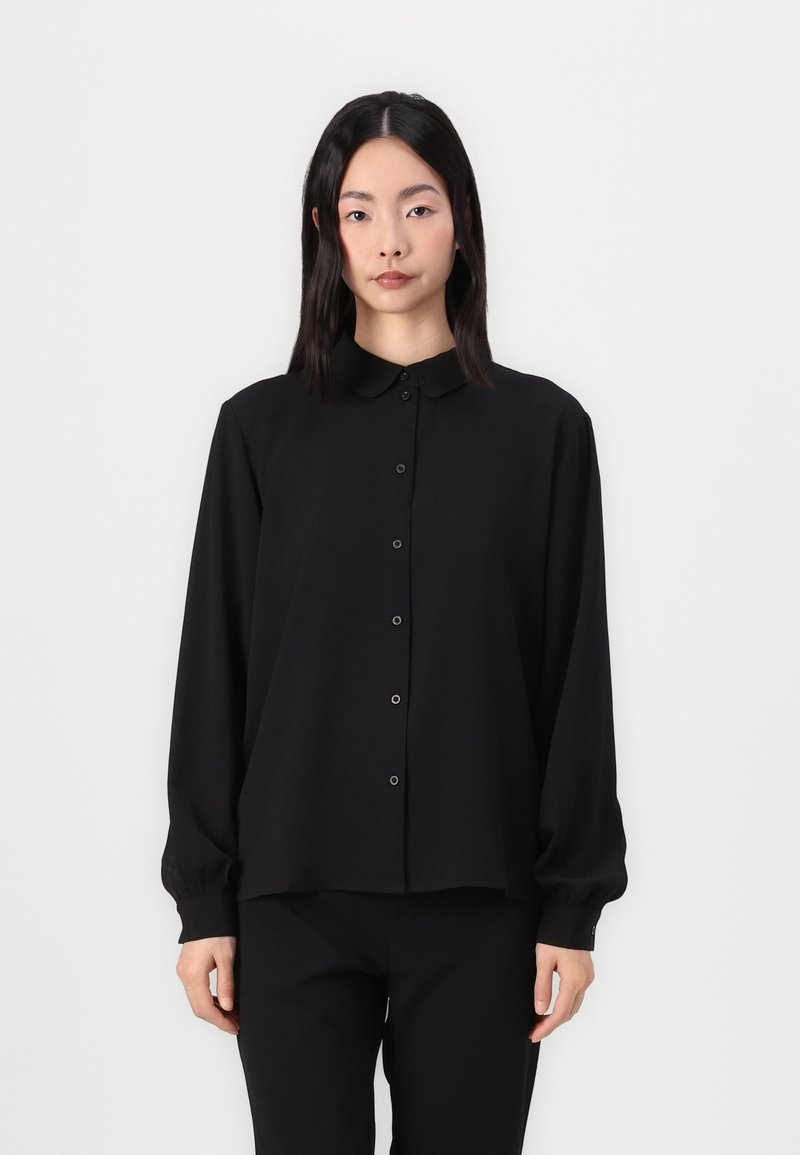 Black long-sleeve shirt with a collar, featuring a straight cut, button closure, and smooth texture. Worn with matching black pants.