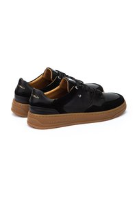 Zapatillas negras que combinan cuero liso y ante, con una suela de goma marrón y un sutil logo en el talón.