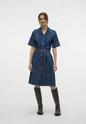 Knoppen-donsen denim jurk met korte mouwen, een ceintuur in de taille en contrasterende stiksels; gecombineerd met kniehoge bruine leren laarzen.