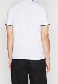 Biała koszulka polo z krótkim rękawem z czarnymi wykończeniami na kołnierzyku i rękawach. Wykonana z bawełny, charakteryzuje się klasycznym krojem i czystym designem.