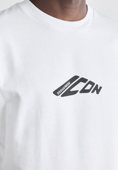 T-shirt en coton blanc avec un logo graphique noir incluant le texte "DSQUARED2" et "CDN", avec un design de police élégant et moderne.