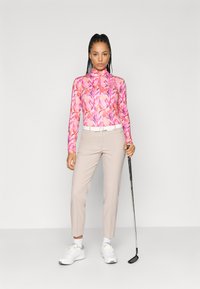 Μακρυμάνικο ροζ λουλουδάτο πουκάμισο γκολφ με φερμουάρ στον γιακά, συνδυασμένο με ανοιχτό μπεζ παντελόνι. Τα αξεσουάρ περιλαμβάνουν μια λευκή ζώνη και ένα μπατζάκι γκολφ.