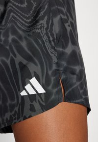 Shorts de sport noirs avec un motif de vague texturé. Présentent une fente sur les côtés et un logo à trois bandes blanches sur l'ourlet.