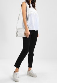 Top blanco sin mangas con detalles de encaje, combinado con pantalones ajustados negros y zapatillas blancas. Bolso cruzado gris con acento de borla.