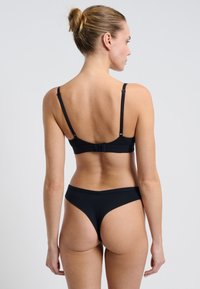 Completo di lingerie nera senza cuciture, con un reggiseno semplice dotato di spalline regolabili e una fascia classica, entrambi in un materiale liscio e elastico.