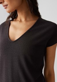 Top nero a maniche corte con scollatura a V. Il tessuto ha una finitura testurizzata, creando una leggera profondità nell'aspetto.