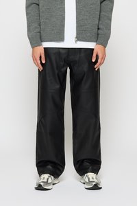 Person som har på seg svarte skinnbukser, grå strikket hettegenser med glidelås, hvit skjorte og hvite joggesko på en hvit bakgrunn.