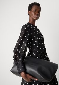 Abito nero con pois, maniche a sbuffo e vita cintrata, abbinato a una borsa a tracolla in pelle nera liscia.