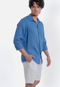 Blauwe linnen long sleeve shirt met een kraag, knopen aan de voorkant en opgerolde mouwen, gedragen met witte linnen shorts, een gladde textuur en een ontspannen pasvorm.