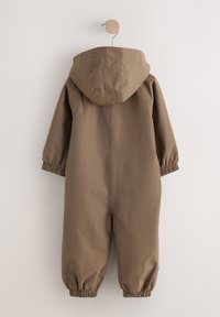 Combinaison imperméable marron avec capuche, poignets élastiques et texture lisse. Présente une coupe décontractée et un design simple, suspendue à un crochet.