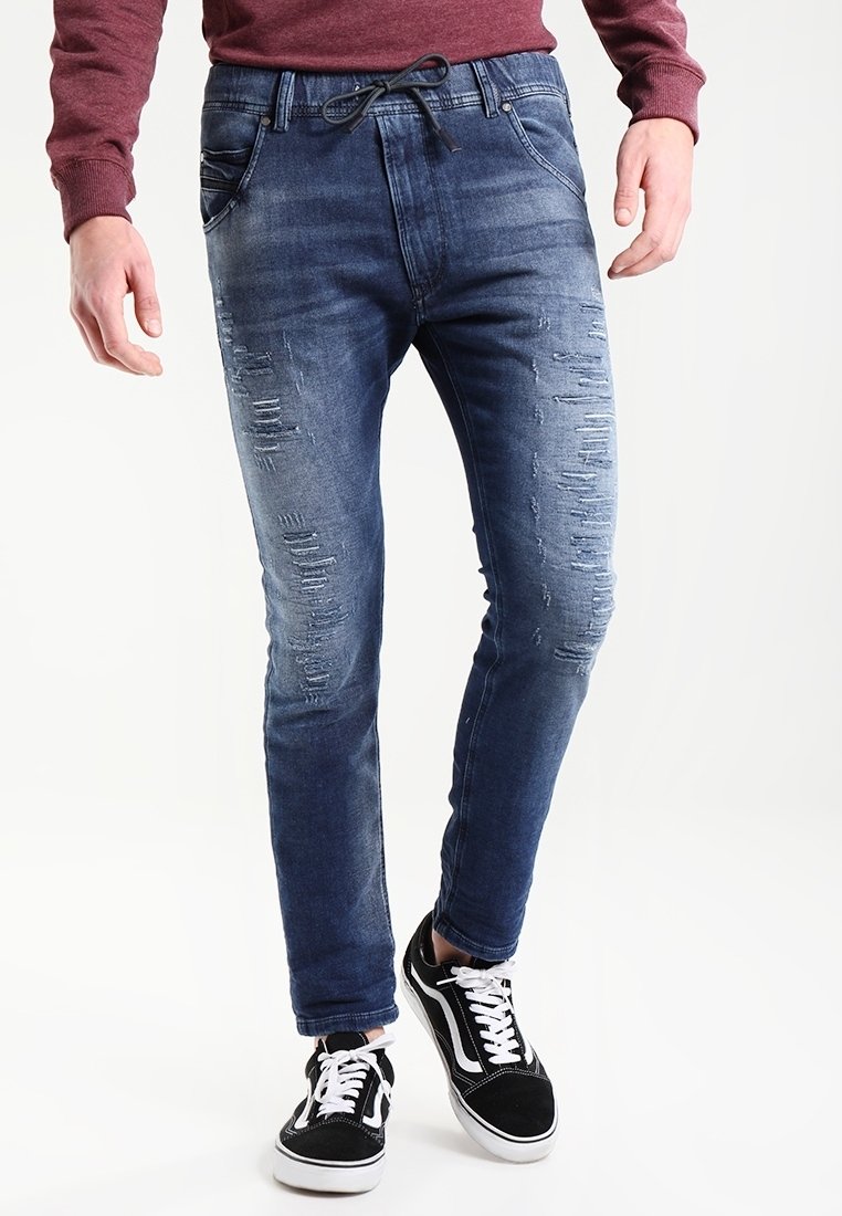 Herrjeans i blå denim med slitna detaljer, avsmalnande passform och drachordmidja. Matchas med svarta sneakers med vita inslag.