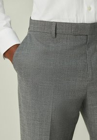 Sivé vzorované nohavice z látky s jemnou mriežkovanou textúrou, vybavené plochým predným dielom, bočnými vreckami a strihaním na mieru.