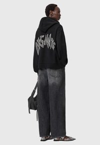 Felpa nera oversize con grafica bianca audace sul retro, abbinata a jeans larghi grigio scuro e ballerine nere a punta. Semplice borsa nera.