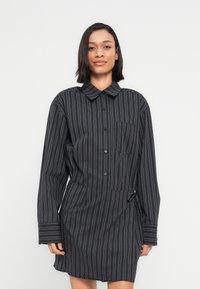 Φόρεμα πουκάμισο με μαύρες και λευκές ρίγες, γιακά, μακριά μανίκια, κούμπωμα με κουμπιά και δέσιμο στη μέση στο πλάι. Απαλό, λείο ύφασμα.