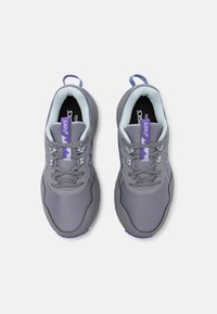 Ténis de atletismo cinzentos com um topo em malha, detalhes em roxo e elementos refletivos. Fecho com atacadores e uma alça no calcanhar para facilitar o uso.