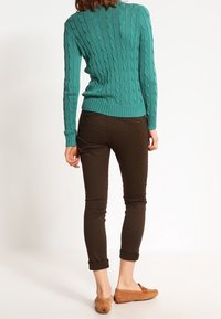 Teal stickad tröja med ribbat mönster, parat med bruna tajta byxor. Bruna uppvikta ärmar och ljusbruna mockaskor.