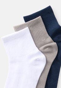 Tri par socksa: bijele, svijetlosive i mornarsko plave. Svaki par ima rebraste manžete i glatku teksturu. Čarape su presavijene kako bi se vidjeli vrhovi.