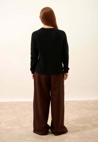 Schwarzer Strickpullover mit einem strukturierten Design, langen Ärmeln und Rundhalsausschnitt, kombiniert mit weiten braunen Hosen. Rückansicht gezeigt.