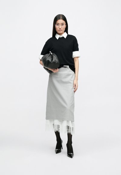 Μαύρο πλεκτό πουλόβερ με άσπρο γιακά πουκαμίσου, γκρι μολυβένια φούστα, δαντελένια λεπτομέρεια στο στρίφωμα, μαύρη τσάντα, μαύρες κάλτσες και ψηλοτάκουνα παπούτσια με αιχμηρή μύτη.