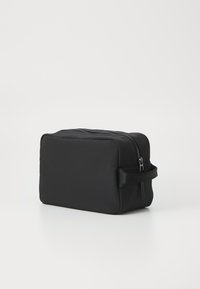 Borsa da toeletta nera rettangolare realizzata in materiale morbido, dotata di una chiusura con zipper superiore e di una maniglia laterale in tessuto per un facile trasporto.