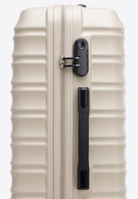 Beige Hartschalenkoffer-Seite mit schwarzem Griff und integriertem Zahlenschloss zur Sicherung der Reißverschlusslaschen.