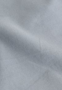 Tessuto grigio chiaro con superficie liscia e strutturata e un delicato motivo a trama diagonale. Nessun motivo visibile o dettagli hardware.